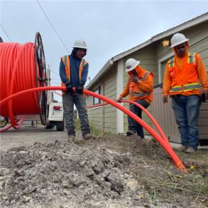 Three construction workers guide conduit into the ground.